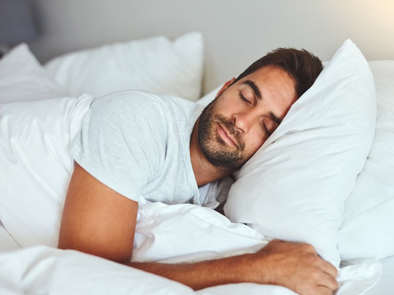 Life Extension, dark haired man with beard and white T-shirt, sleeping peacefully in a bed with white sheets